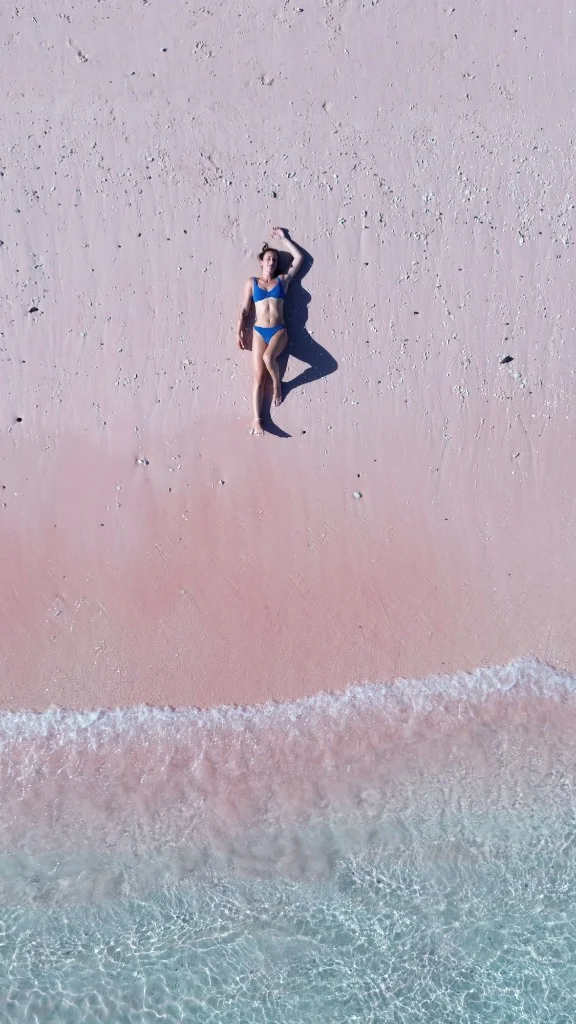 Top-down drone shot of a tourist relaxing on the unique pink sand of Komodo National Park